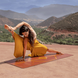 Yoga matı üzerindeki mozaik deseniyle dağ manzarasında esneme yapan kadın. Toprak tonlarında çevre dostu yoga minderi.