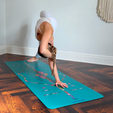 Liforme Tropical Paradise Yoga matı üzerinde beyaz giysili kadın forward fold pozisyonunda egzersiz yapıyor.